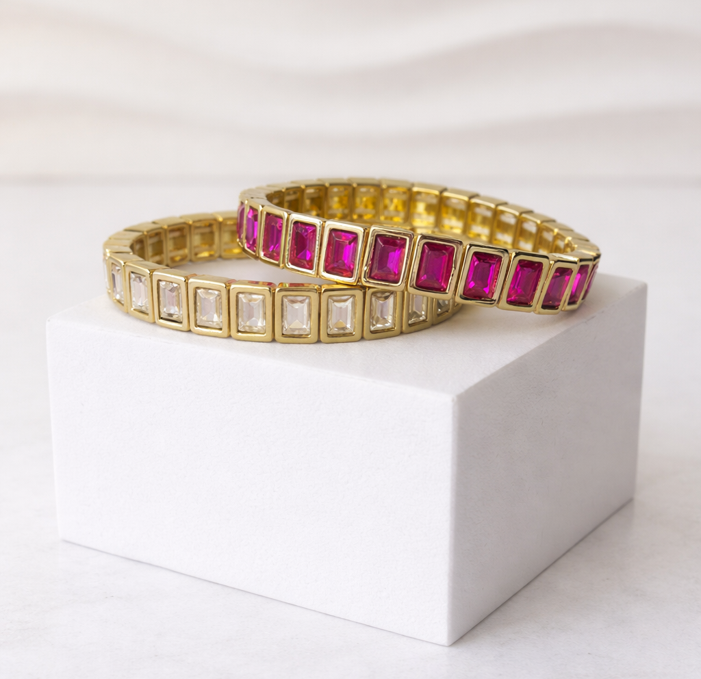 Gold bracelets with pink and clear gemstones on a white surface