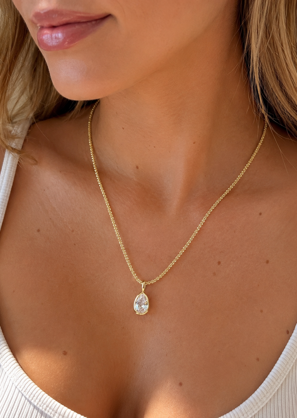 Model wearing a gold teardrop cubic zirconia pendant necklace on a delicate gold chain.