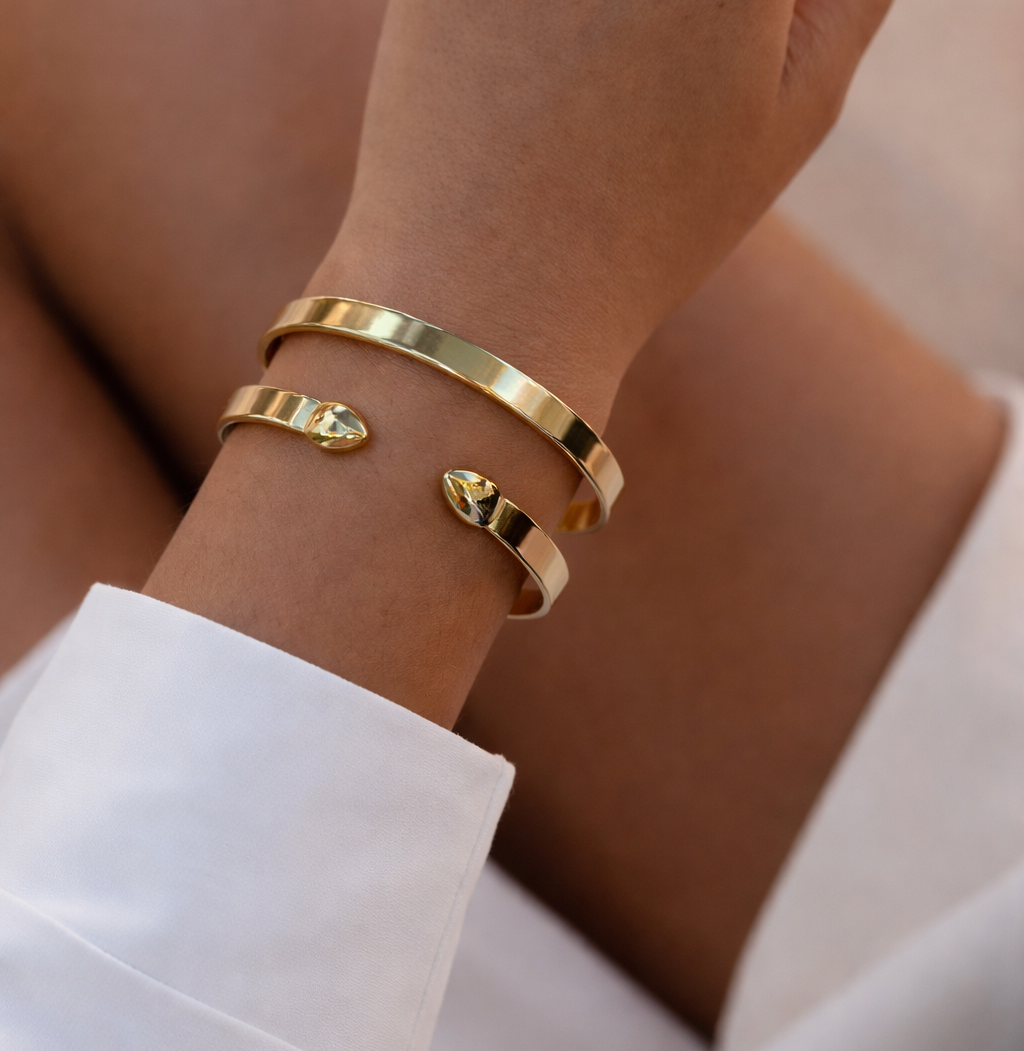 Gold cuff bracelets on a wrist with a blurred background