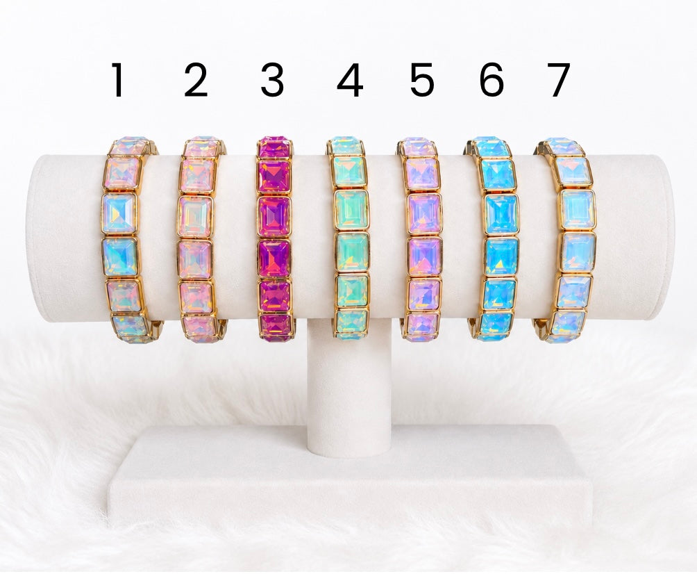 Pastel crystal stretch bracelets displayed on a white jewellery stand, featuring rectangular crystal stones in aqua, pink, lavender, blue, and iridescent tones with gold-tone accents.