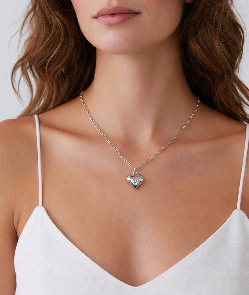 Woman wearing a silver necklace with a heart pendant on a plain background