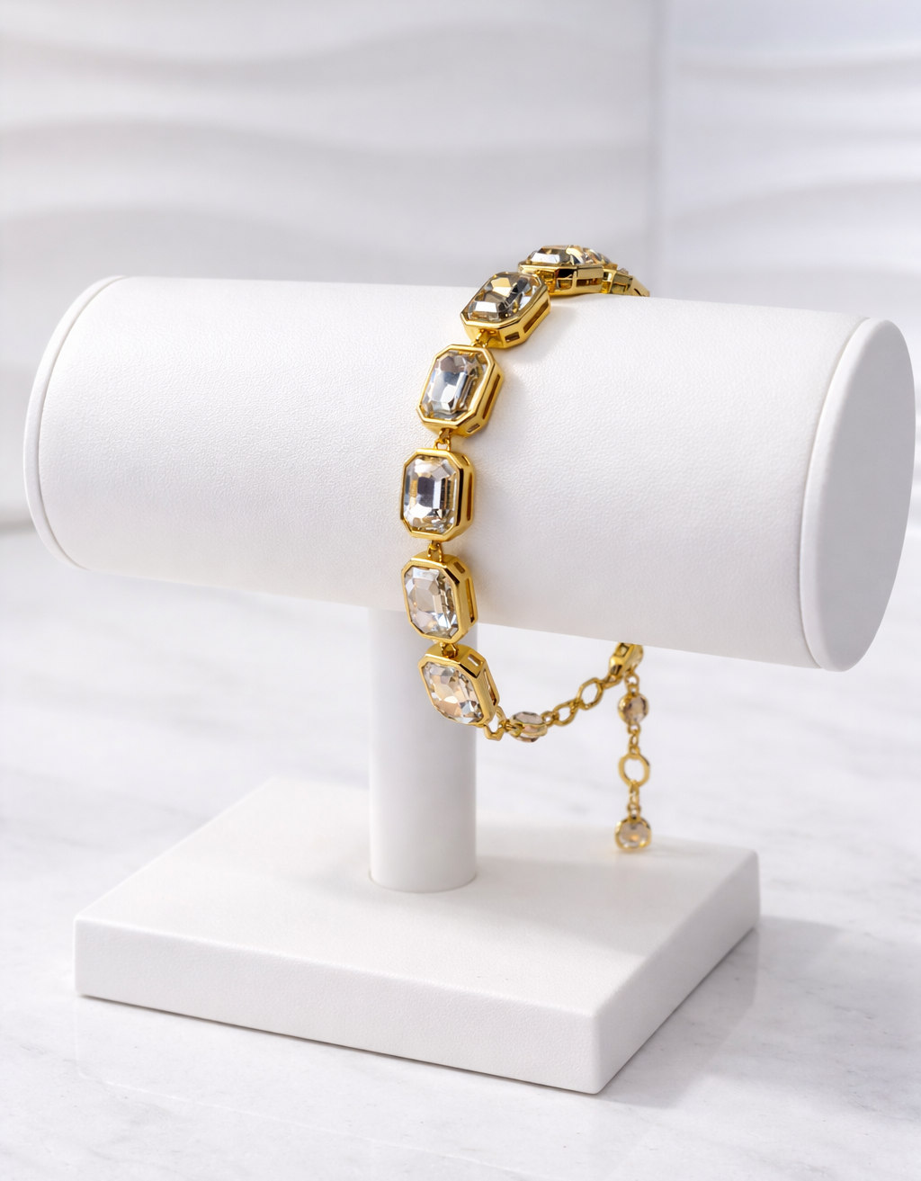 Gold bracelet with emerald cut golden stones on a white stand against a white background