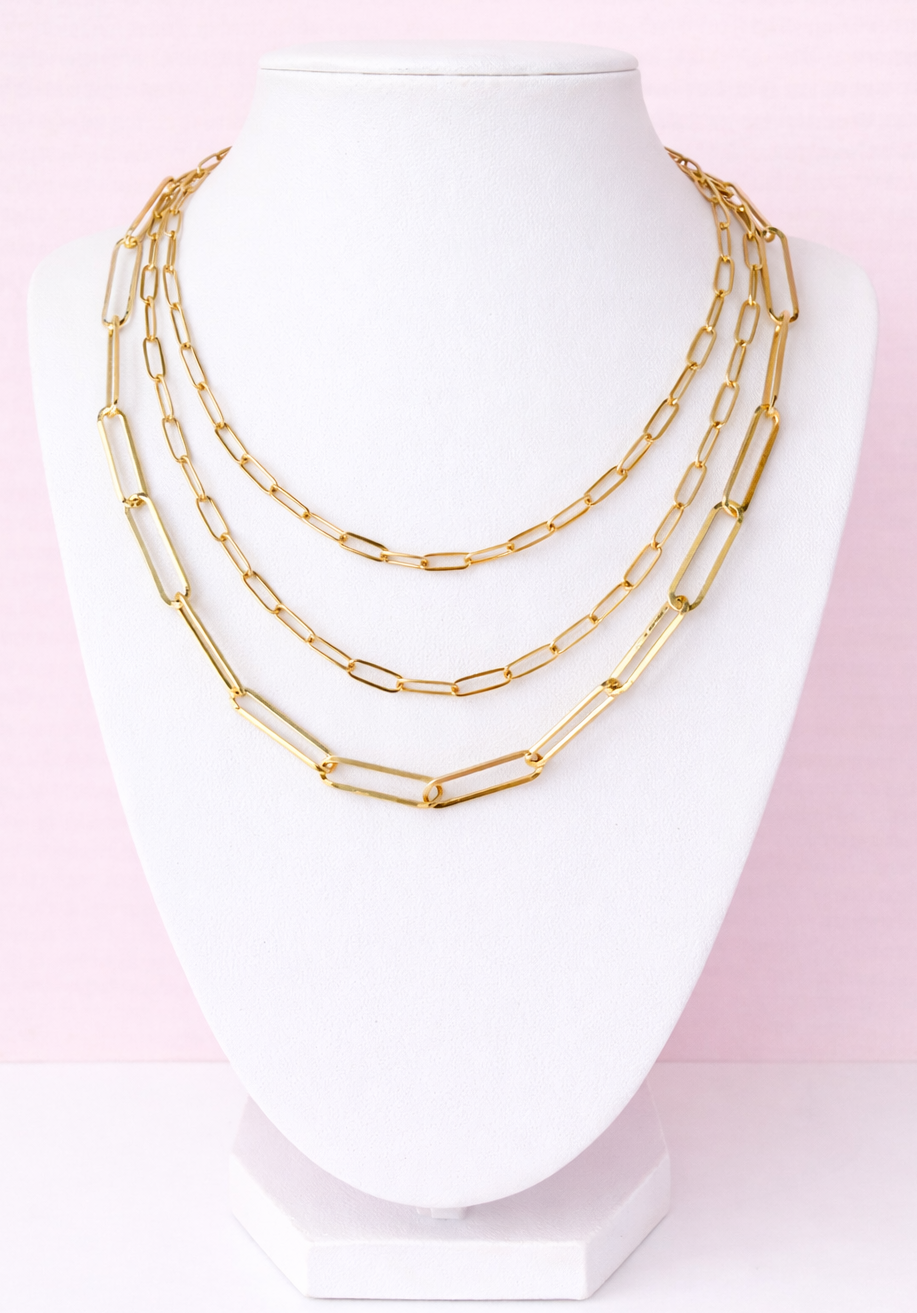 Gold layered chain necklace on a mannequin bust against a pink background