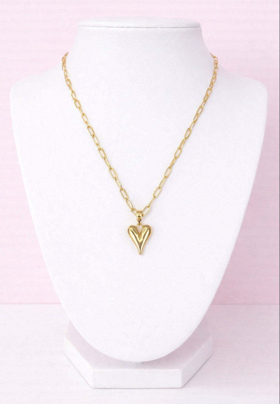 Gold necklace with a heart charm on a mannequin against a pink background