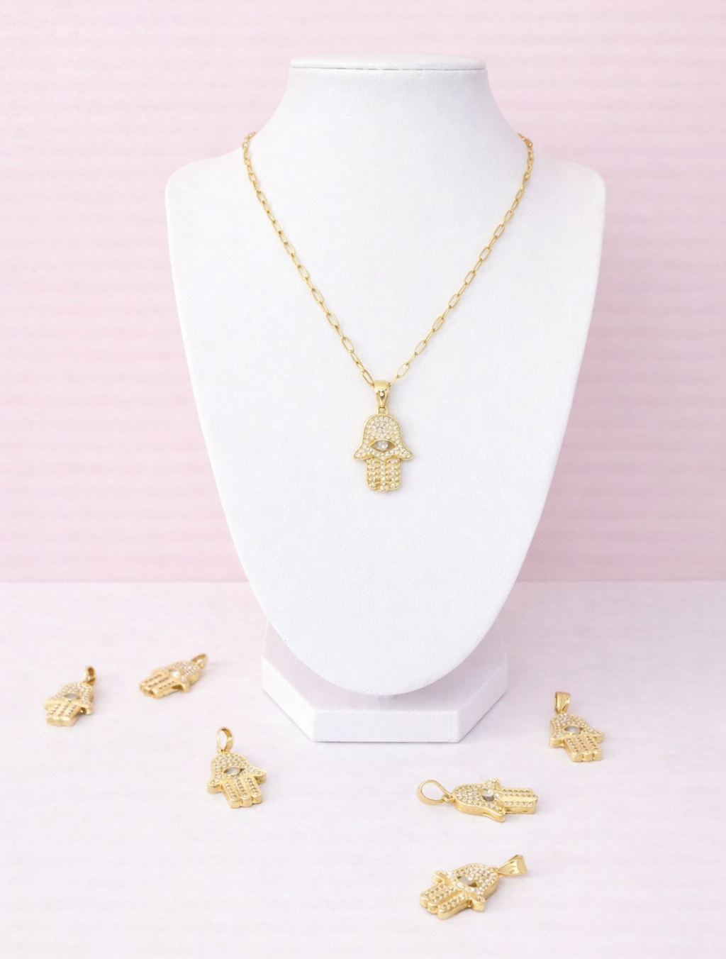 Gold hamsa charm on a white mannequin bust against a pink background