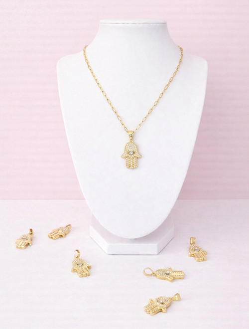 Gold hamsa charm on a white mannequin bust against a pink background