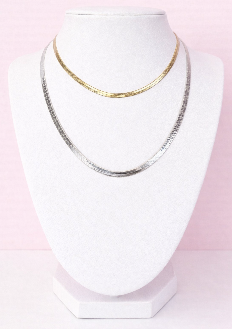 Two herringbone necklaces on a white mannequin bust against a pink background