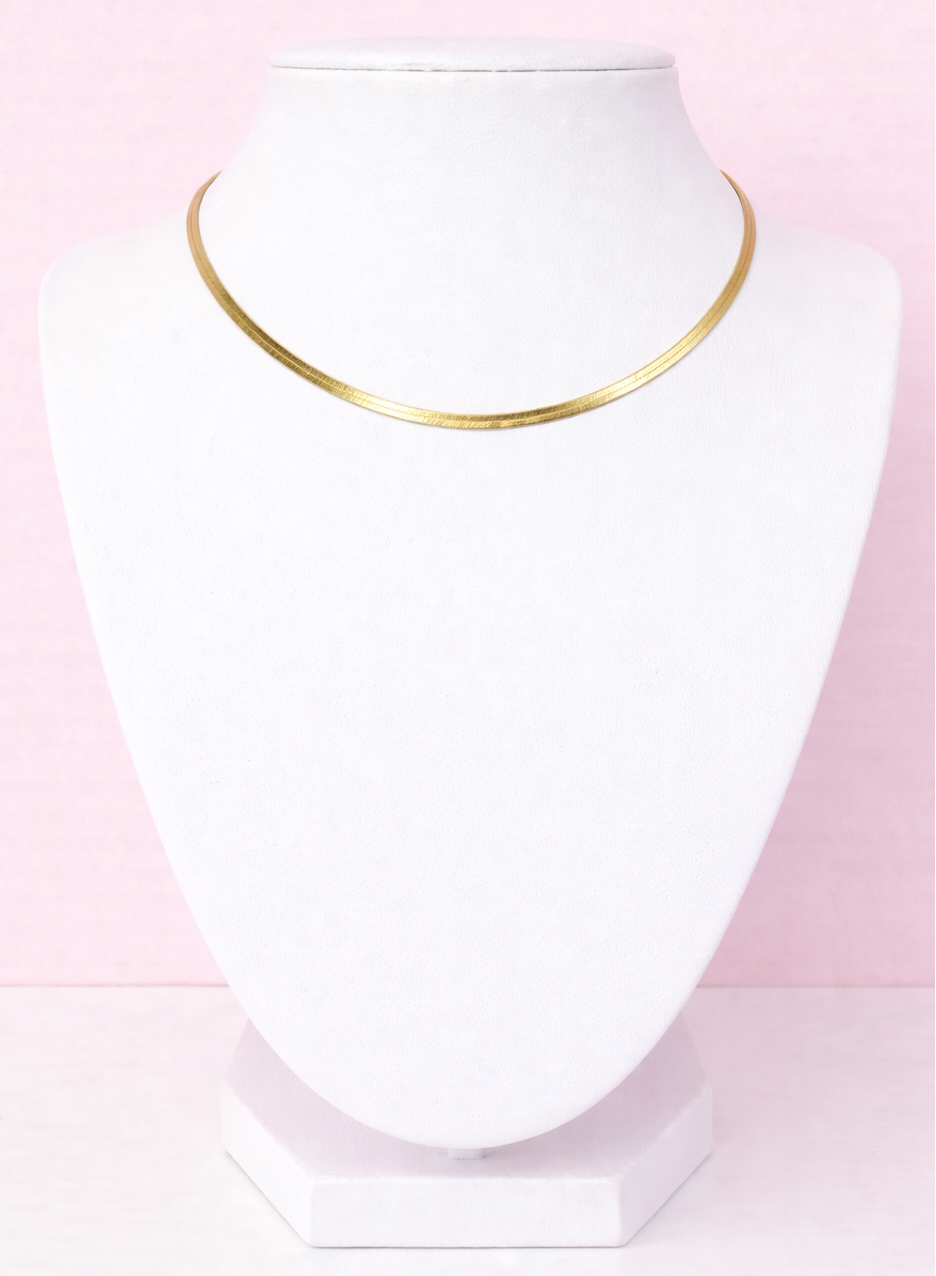 Gold herringbone necklace on a white mannequin bust against a pink background