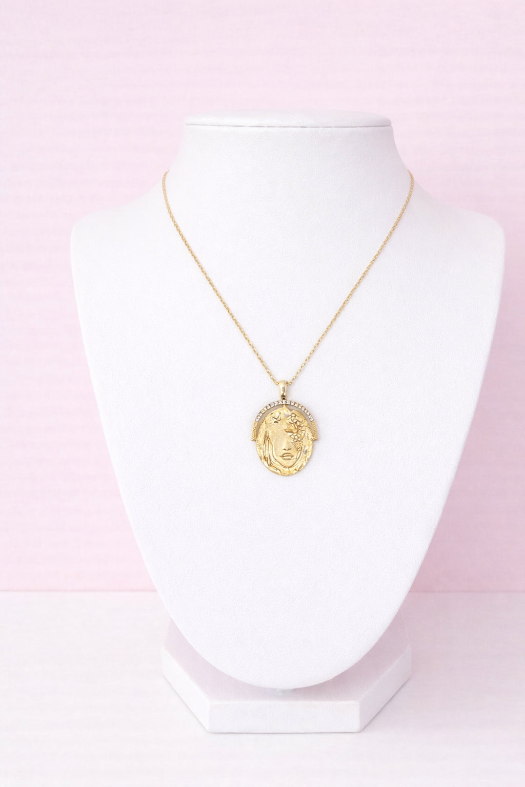 Gold necklace with a pendant on a white mannequin against a pink background