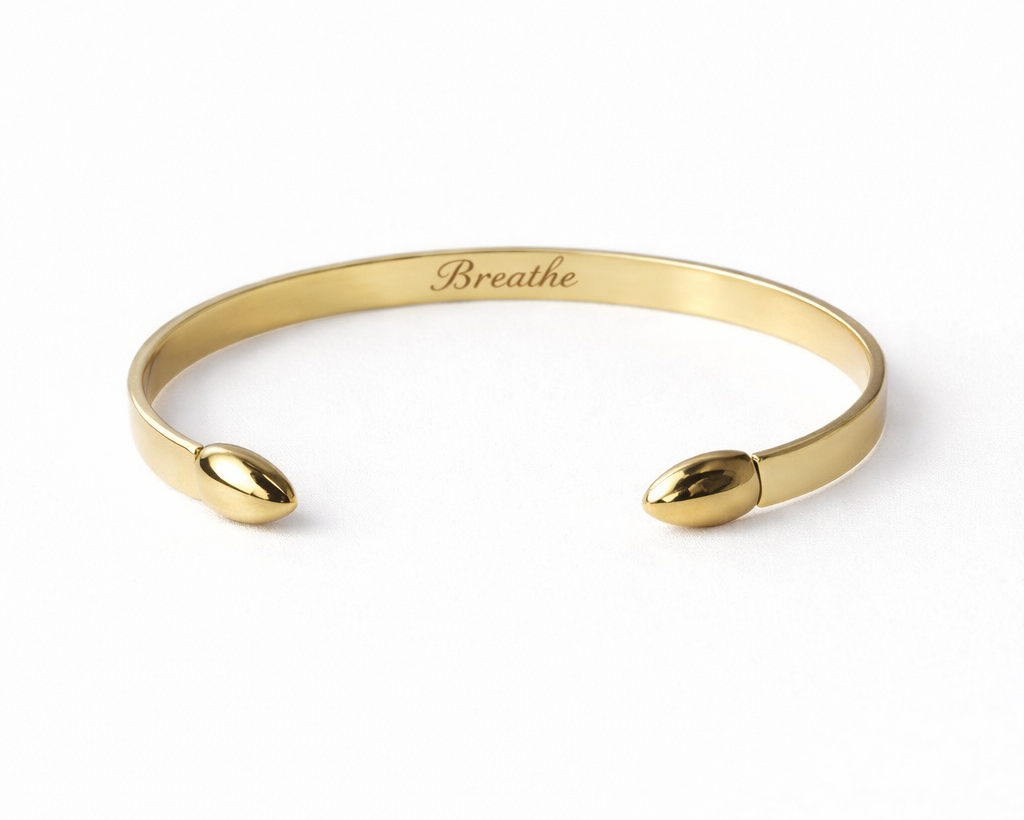 Gold bracelet with 'Breathe' engraving on a white background