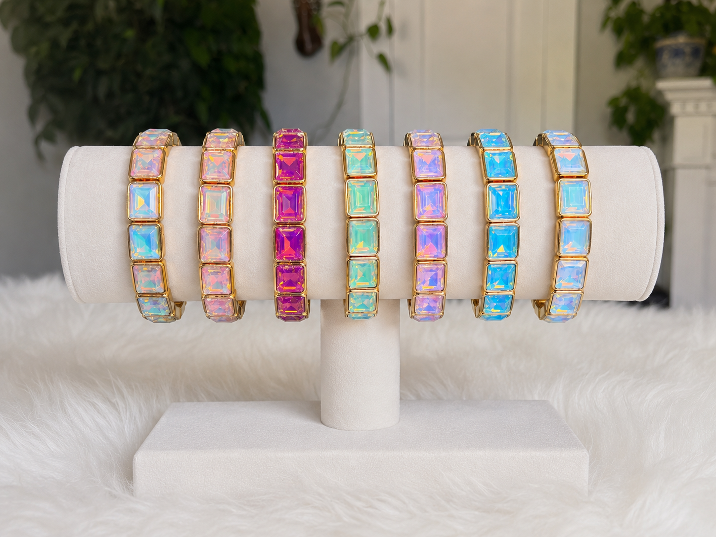 Stack of pastel crystal stretch bracelets in gold-tone settings, featuring pink, aqua, lavender, blue, and iridescent rectangular stones.