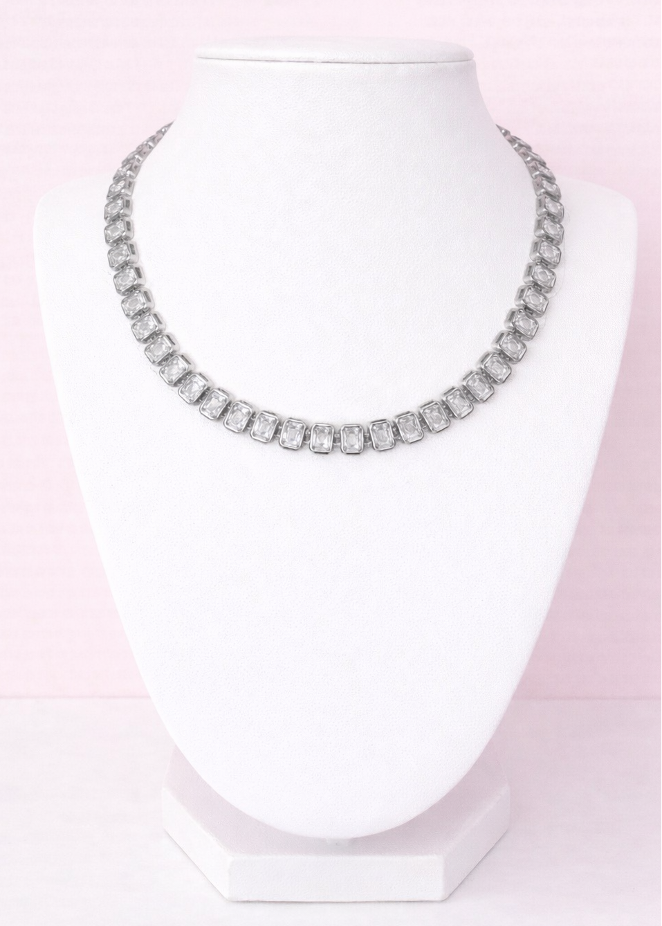 Silver tennis necklace on a mannequin bust against a pink background