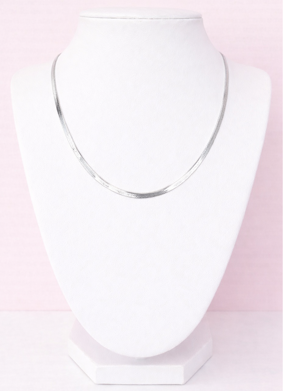 Silver herringbone necklace on a white stand against a pink background