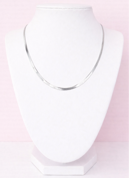 Silver herringbone necklace on a white stand against a pink background