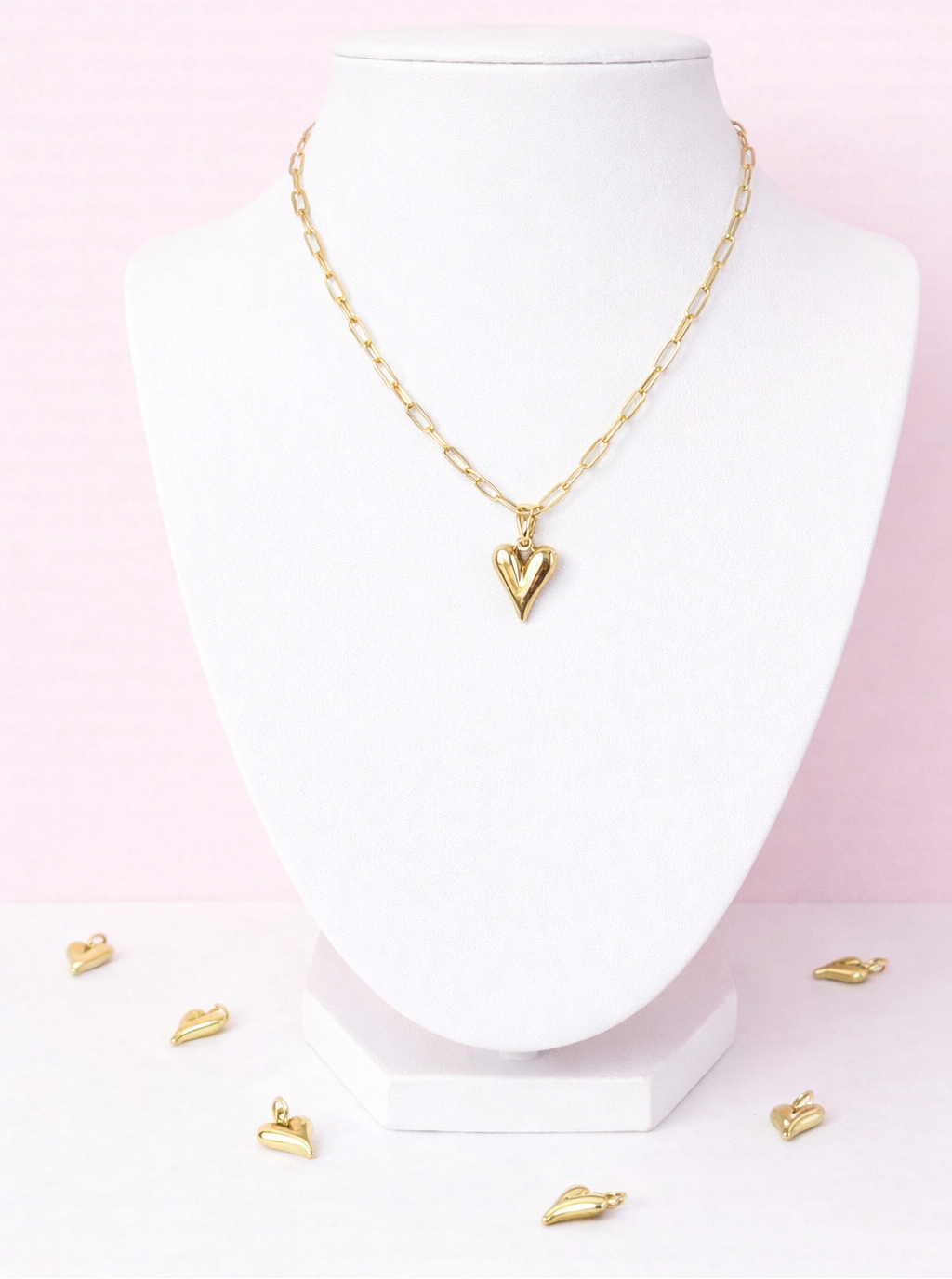 Gold necklace with heart charm on a mannequin bust against a pink gradient background