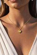 Gold heart-shaped pendant necklace on a model wearing a white top.