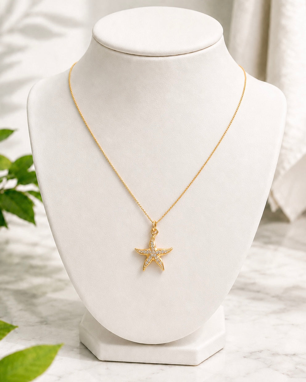 Gold seastar charm pendant with cubic zirconia accents displayed on a white jewellery bust.