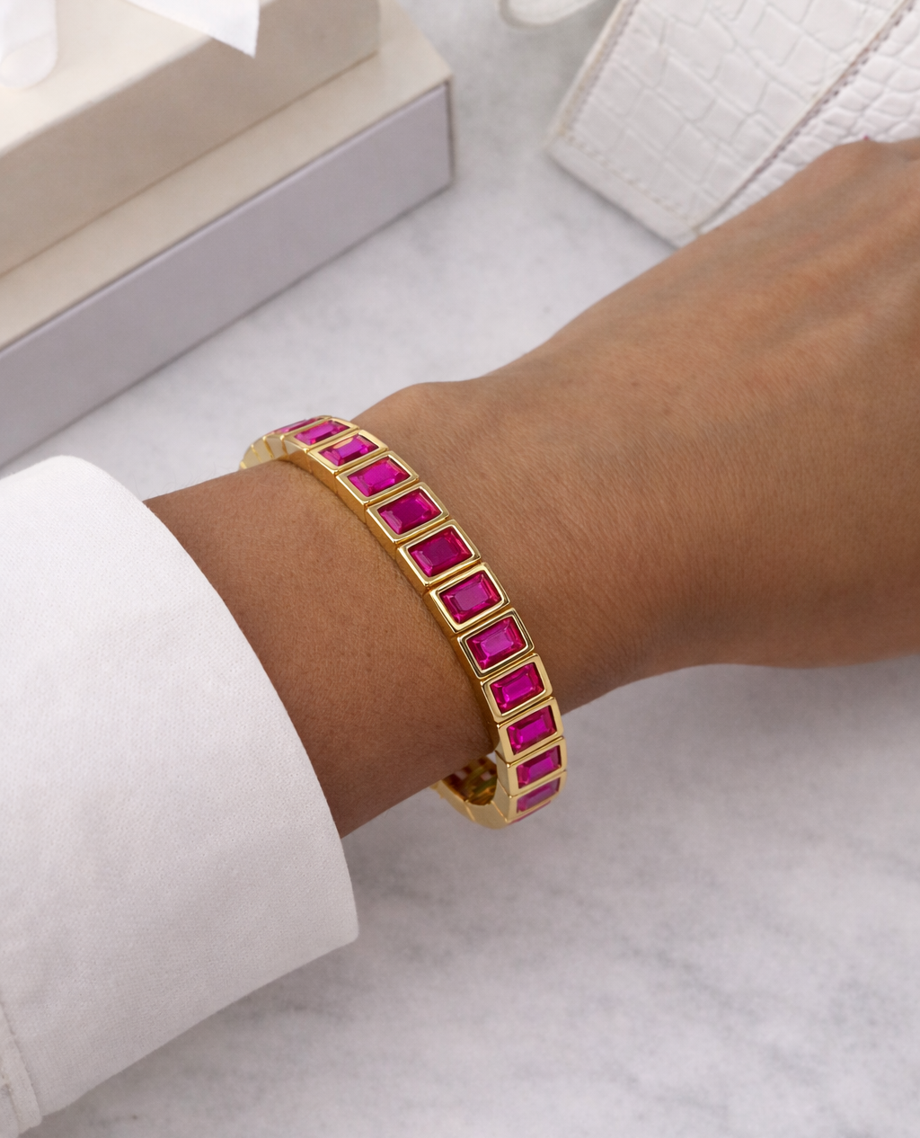 Gold bracelet with pink stones on a wrist against a neutral background