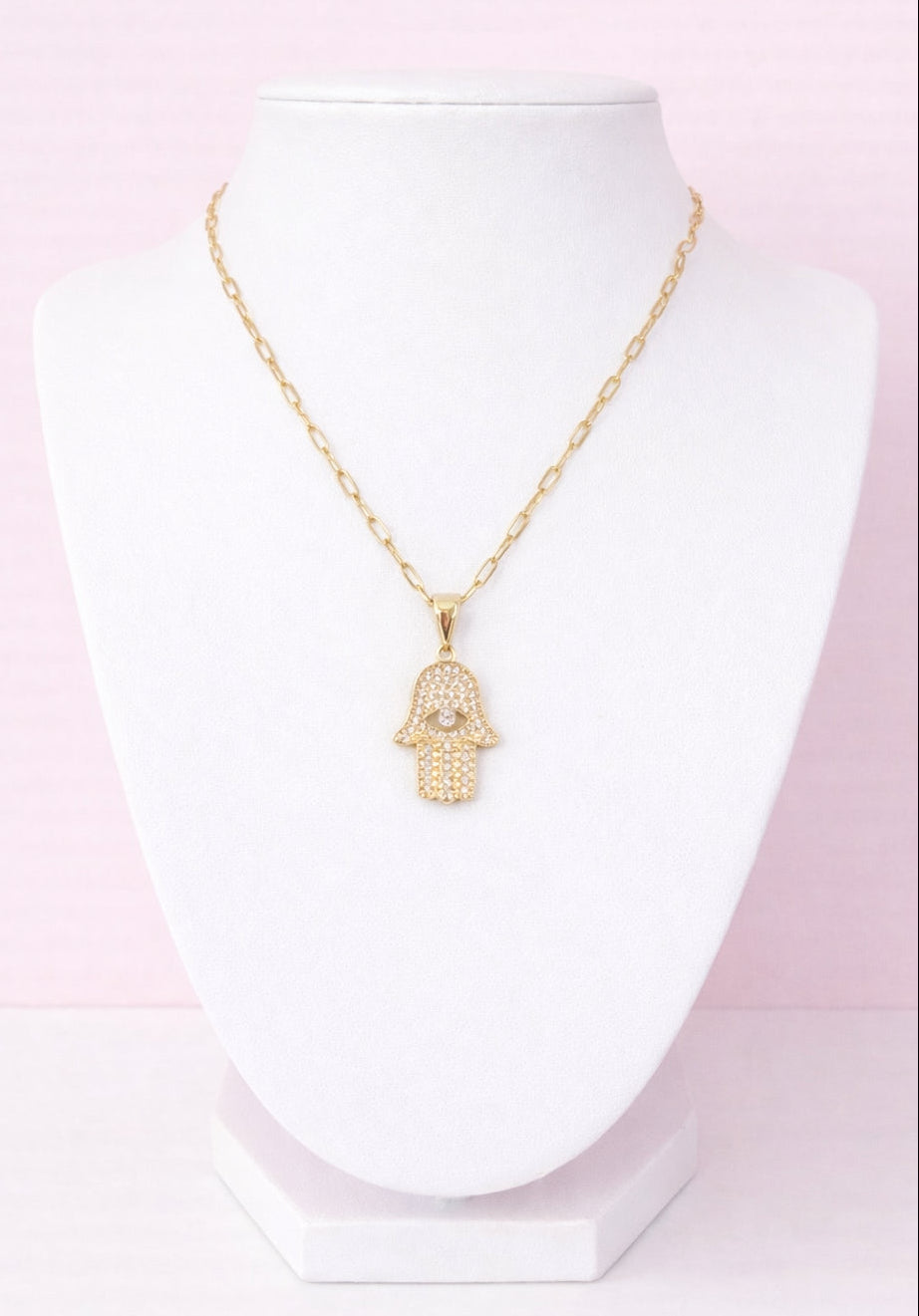 Gold necklace with a hamsa hand pendant on a white mannequin against a pink gradient background
