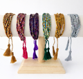 Set of colorful beaded bracelets with tassels on a wooden stand against a white background