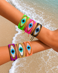 Colorful miyuki evil eye beaded bracelets on a person's wrist with a beach background
