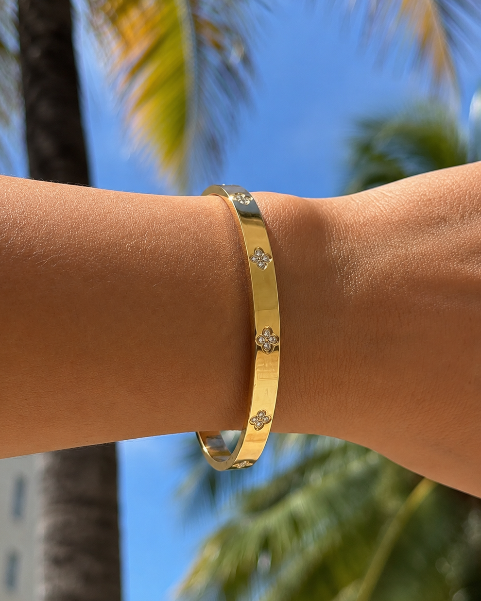 Starlight gold stainless steel bangle bracelet with sparkling cubic zirconia clover details on a model’s wrist.