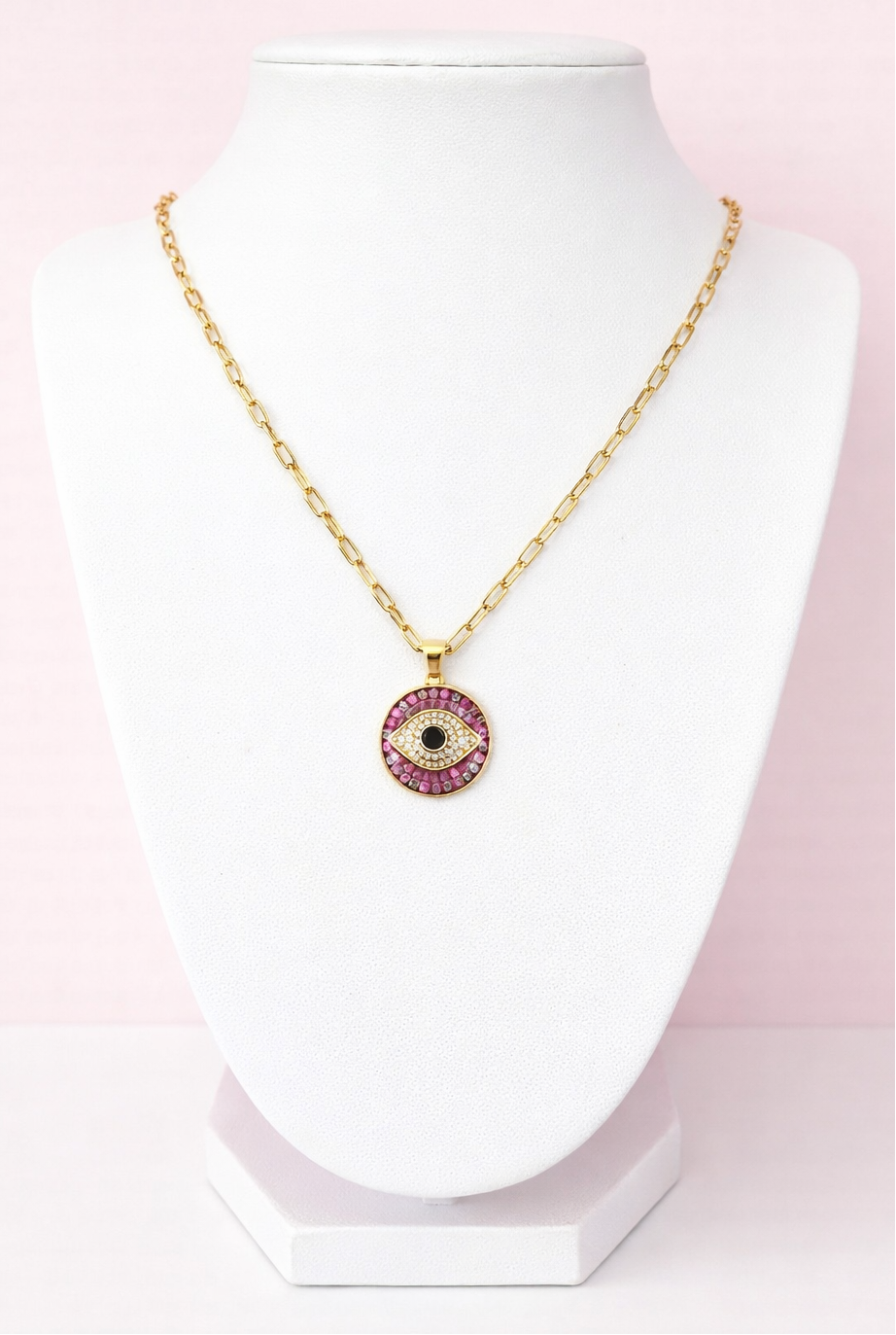 Gold necklace with a pink evil eye pendant on a white mannequin against a pink background