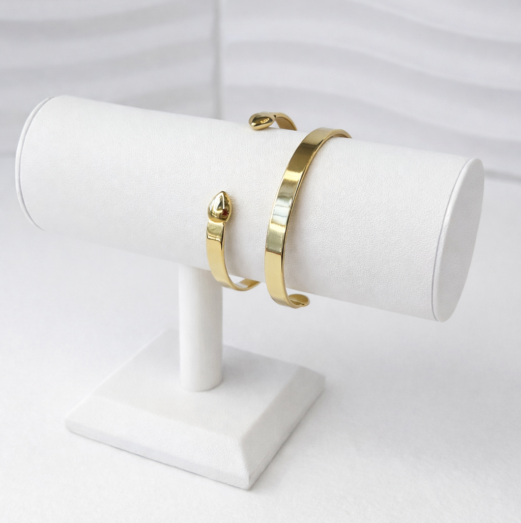 Gold cuff bracelets on a white stand against a light gray background