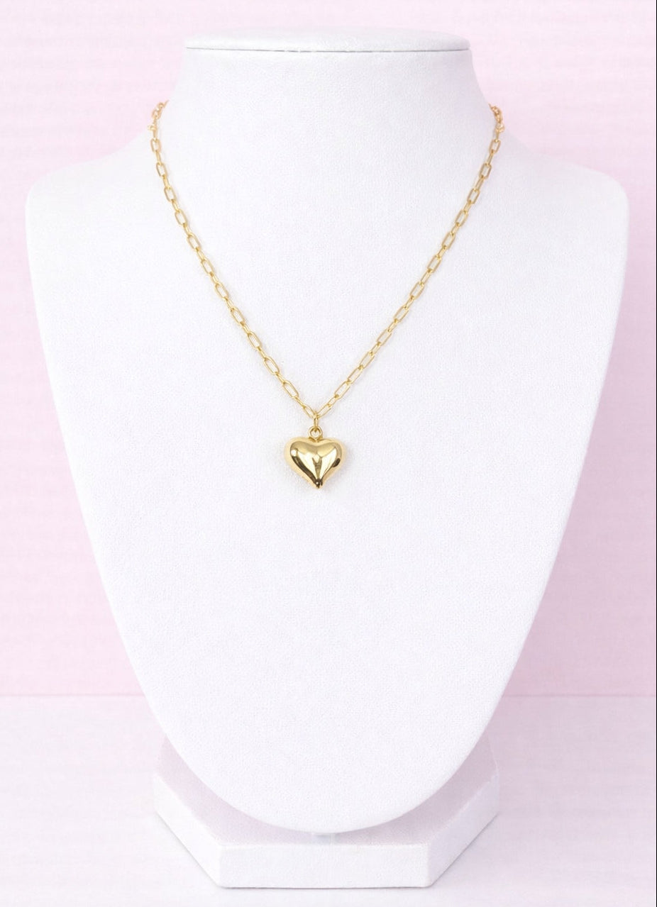 Gold heart-shaped pendant necklace on a mannequin bust with a pink gradient background