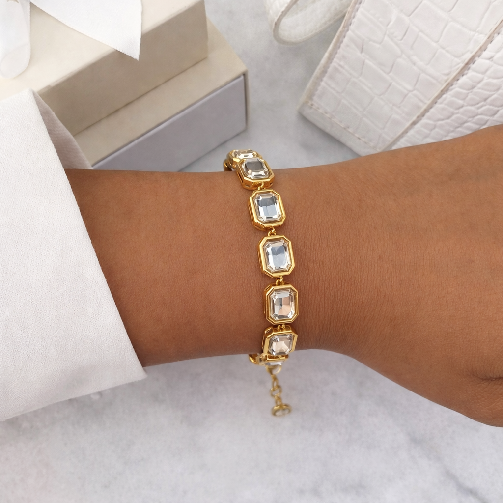 Gold bracelet with emerald cut gemstones on a wrist against a neutral background
