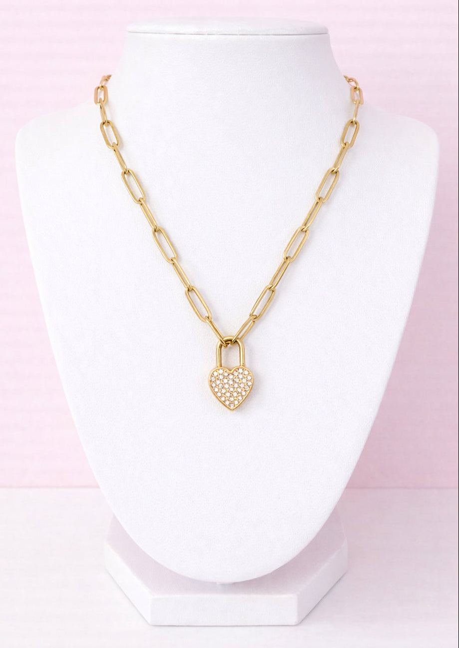 Gold chain necklace with a heart lock pendant on a mannequin against a pink background