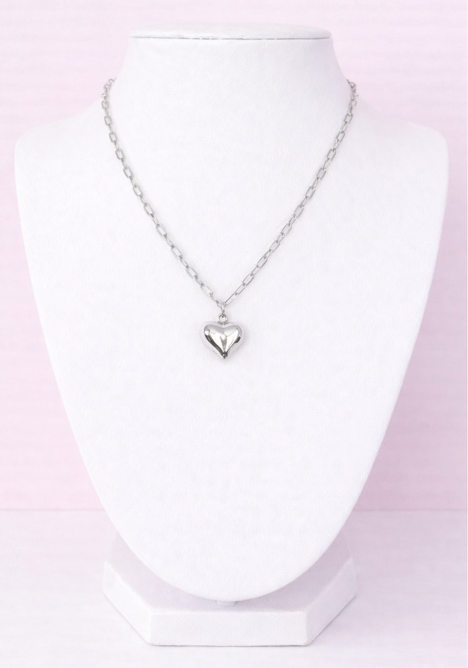 Silver heart-shaped pendant necklace on a mannequin bust against a pink background