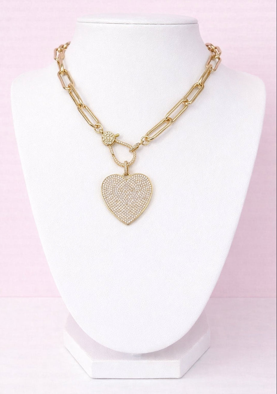 Gold pavé heart-shaped pendant necklace on a white mannequin bust against a pink background