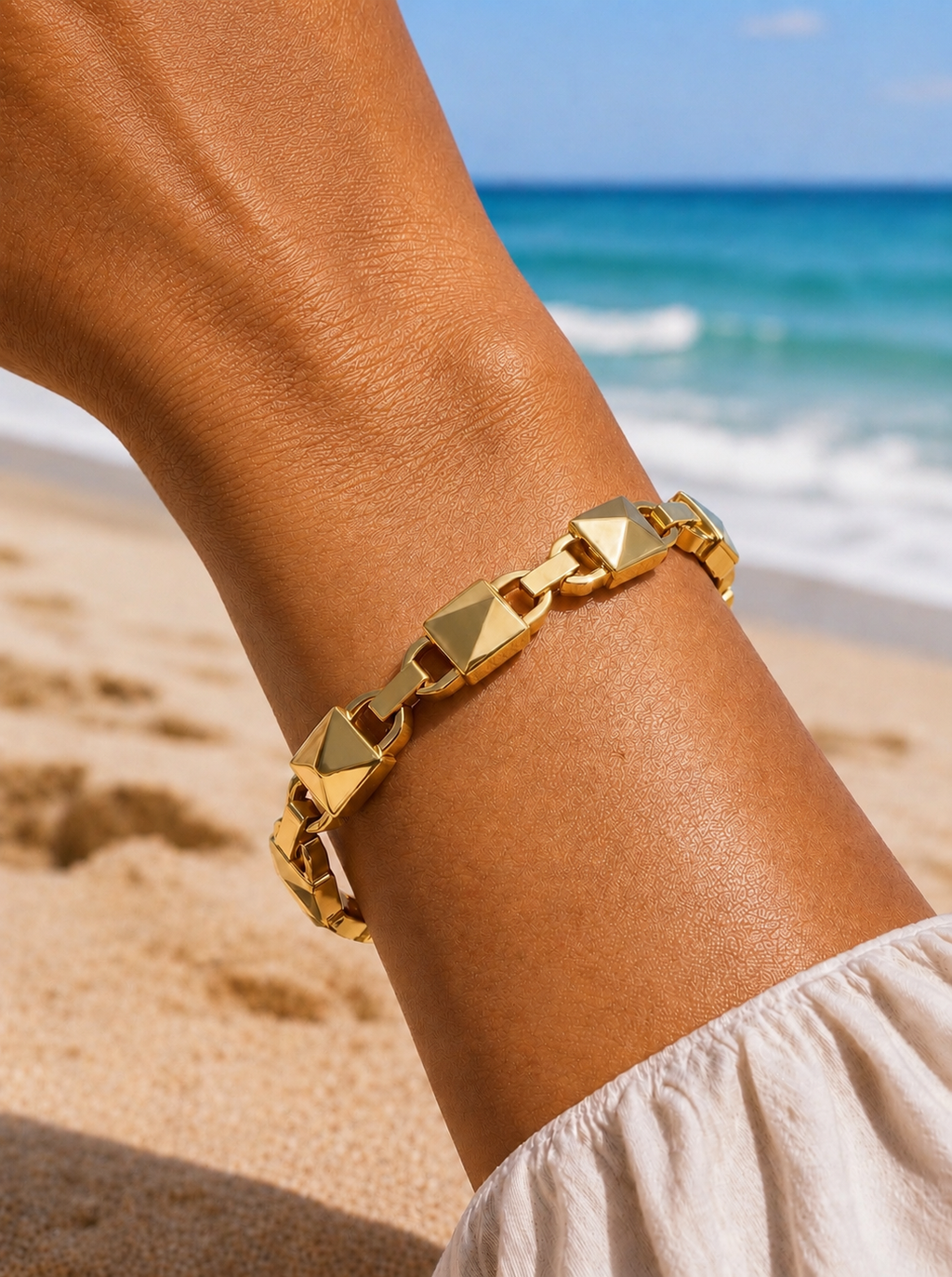Bailey Bangle in 18k gold plating worn on wrist at the beach, waterproof stainless steel cuff bracelet with polished geometric links.