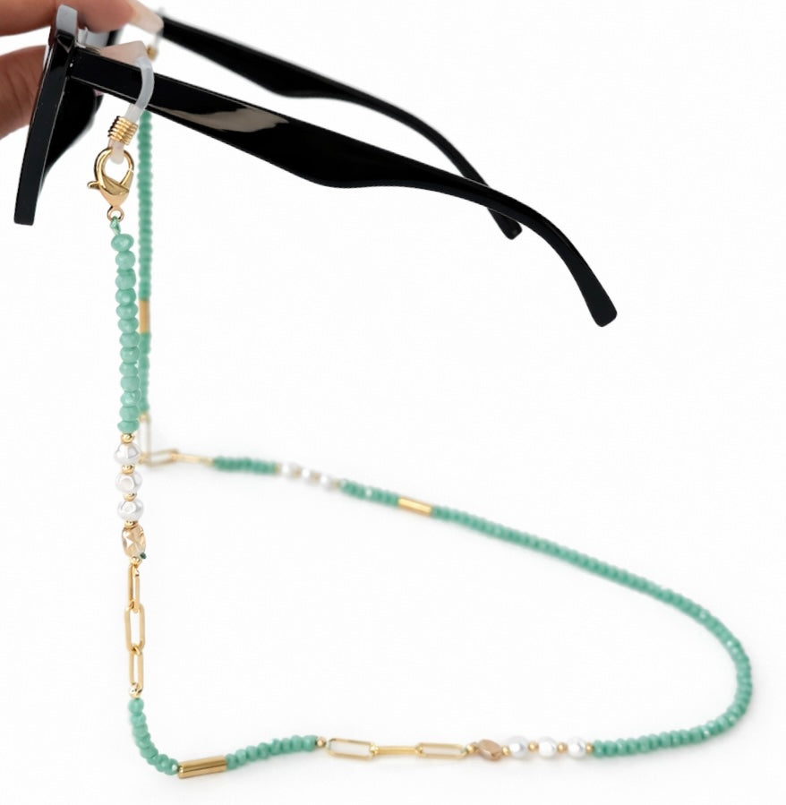 Green beaded eyeglass chain draped over a pair of black sunglasses on a white background