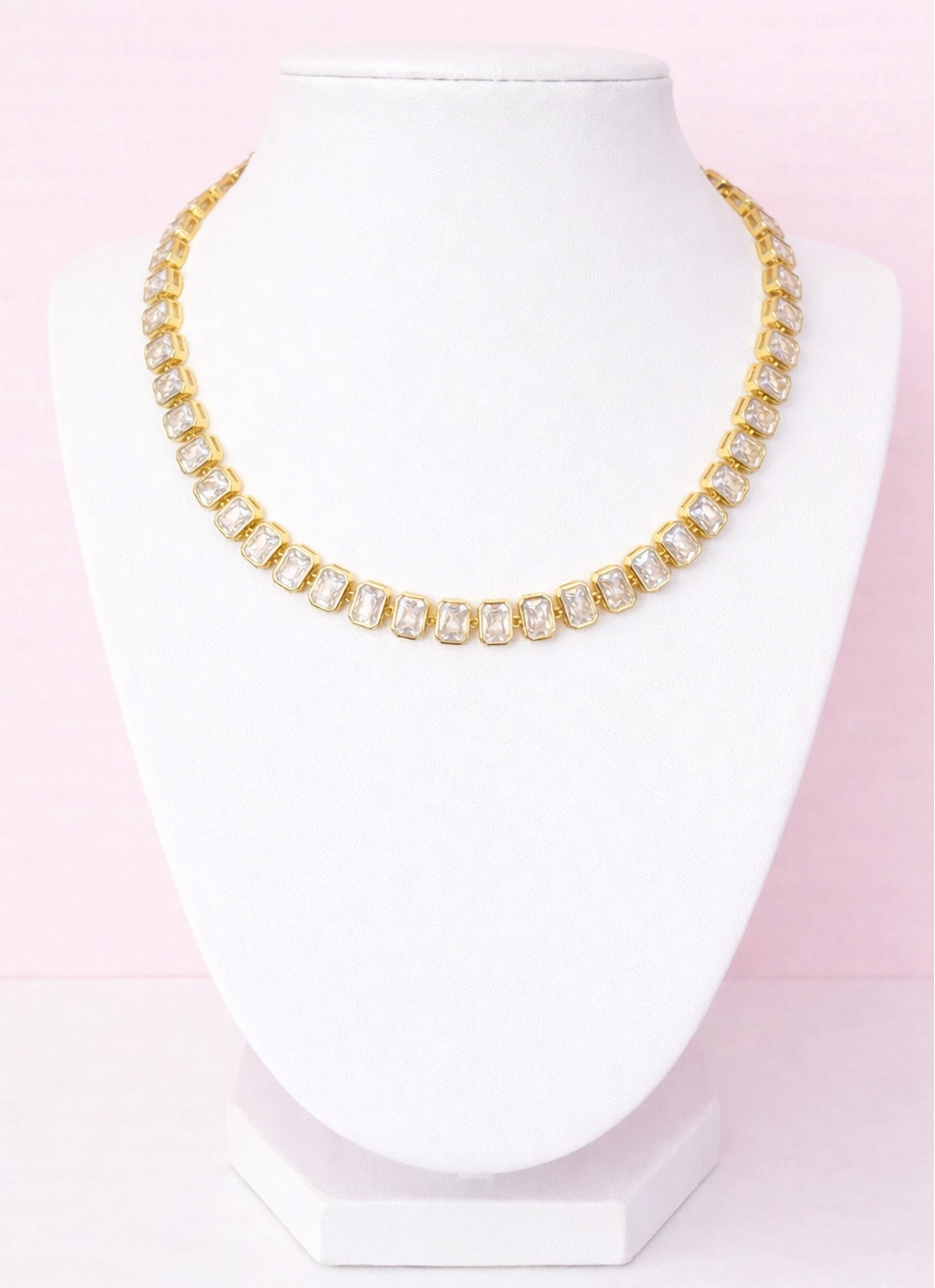 Gold tennis necklace on a mannequin head against a pink background