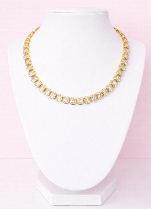 Gold tennis necklace on a mannequin head against a pink background