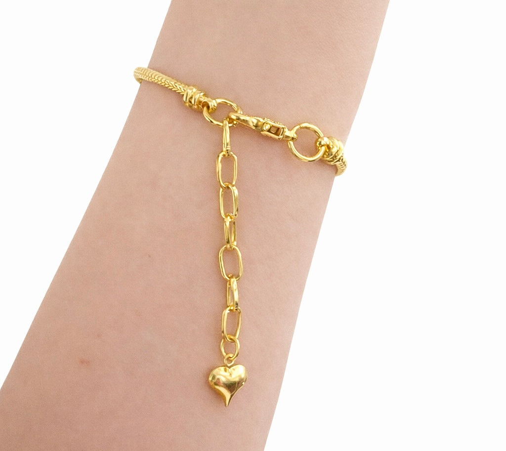 Gold chain bracelet with a heart-shaped charm on a wrist against a white background