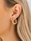 Gold twisted chunky hoop earrings worn on a model’s ear with a polished finish.