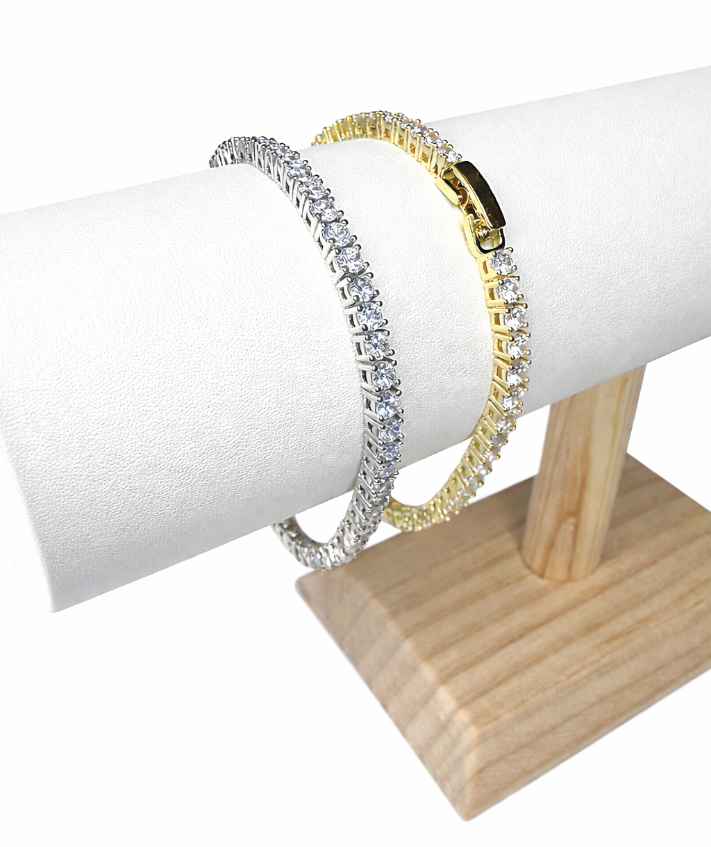 Two tennis bracelets, one gold and one silver, on a stand with a white background