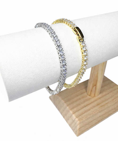 Two tennis bracelets, one gold and one silver, on a stand with a white background