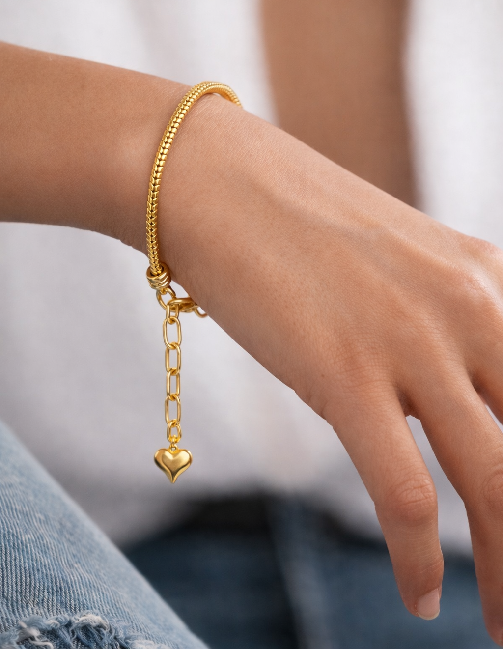 Gold snake charm chain charm bracelet with heart charm and adjustable extension worn on woman’s wrist