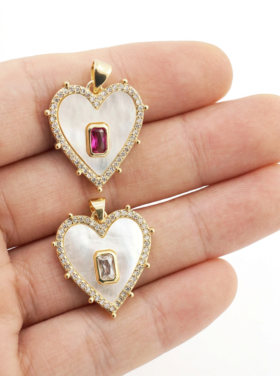 Heart-shaped pendants with gemstones held between fingers on a white background