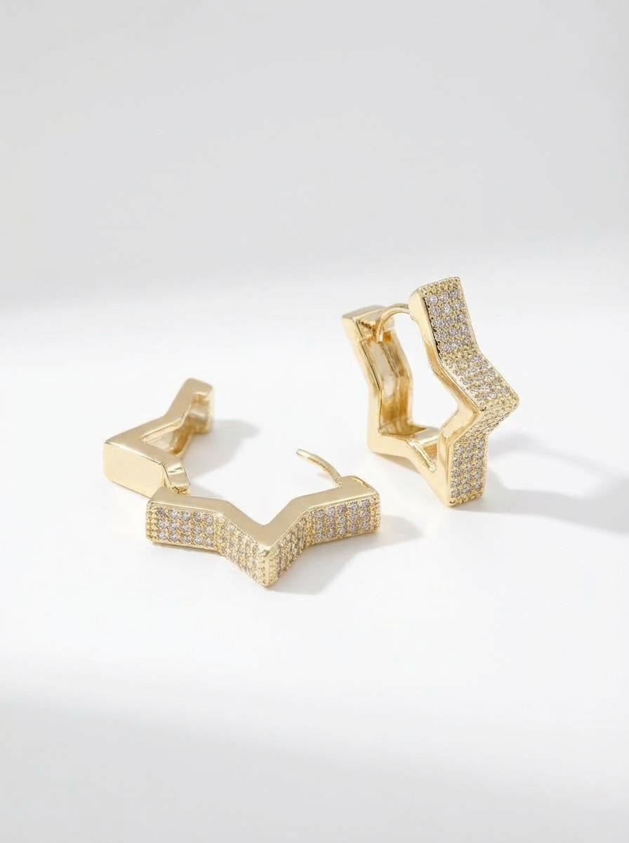 Gold star huggie earrings with zirconia detailing on a white background