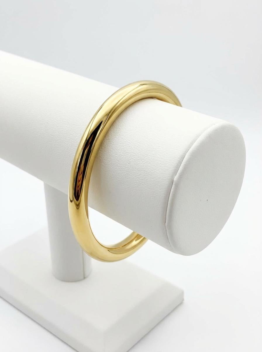 Gold-tone hollow bangle bracelet displayed on white jewellery stand