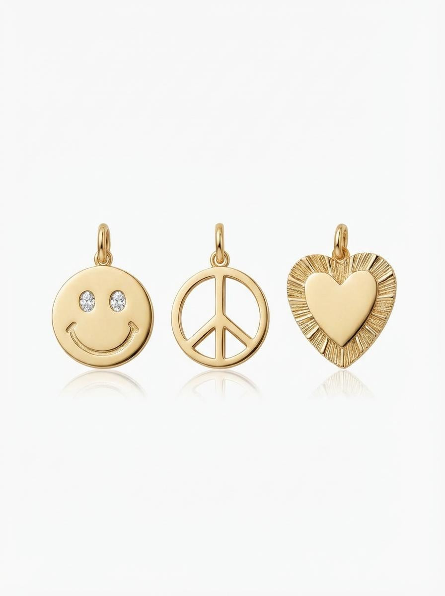 Gold tone charm pendants, featuring a smiley face, peace symbol, and textured heart on a white background