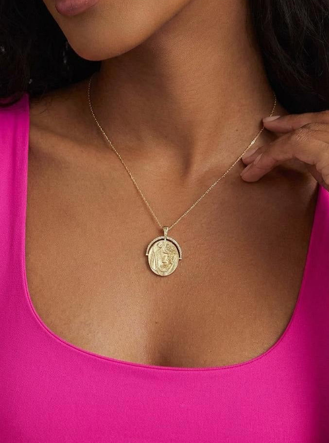 Model wearing a gold plated, oval pendant, necklace with detail and pearl accent