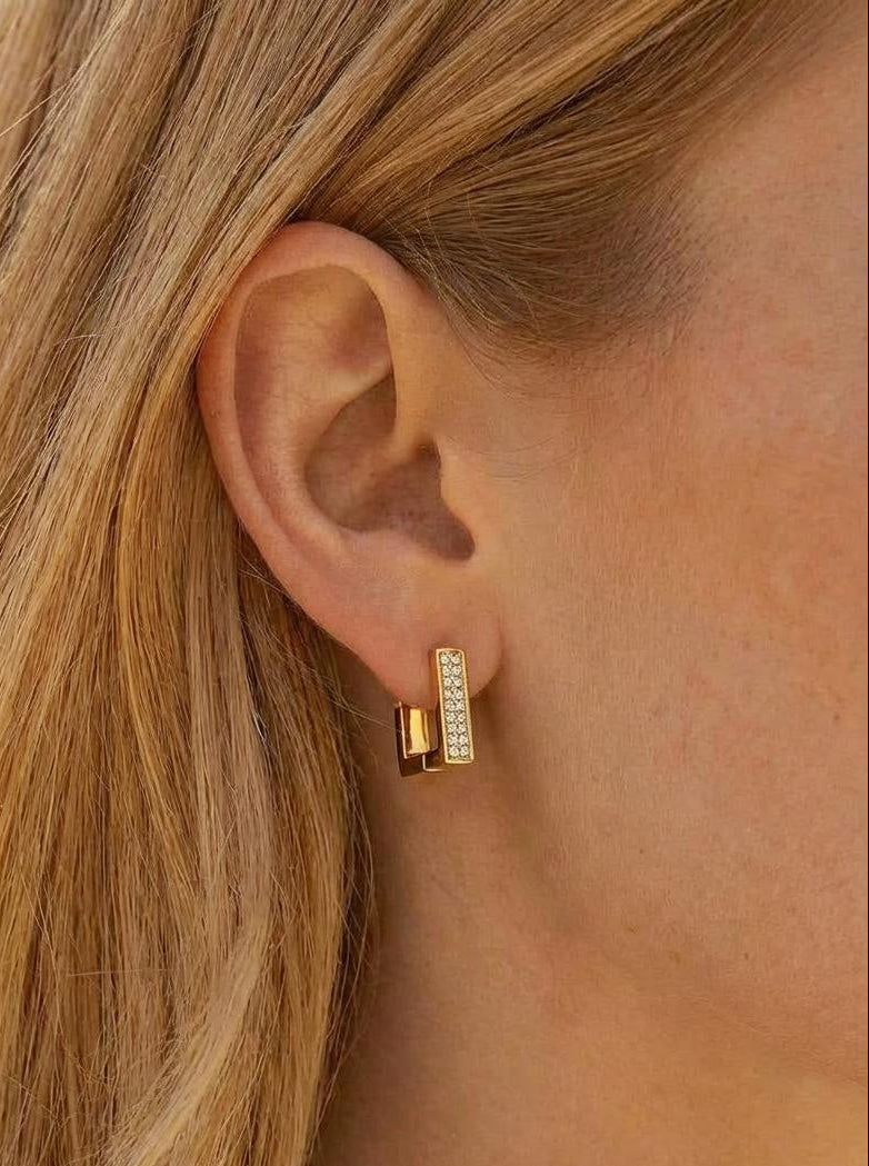 Pair of gold plated square hoop earrings on neutral background