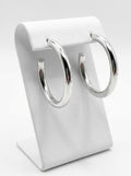 White gold plated hoop earrings with smooth rounded silhouette on display stand