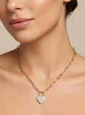 Woman wearing a gold necklace with a heart pendant against a neutral background